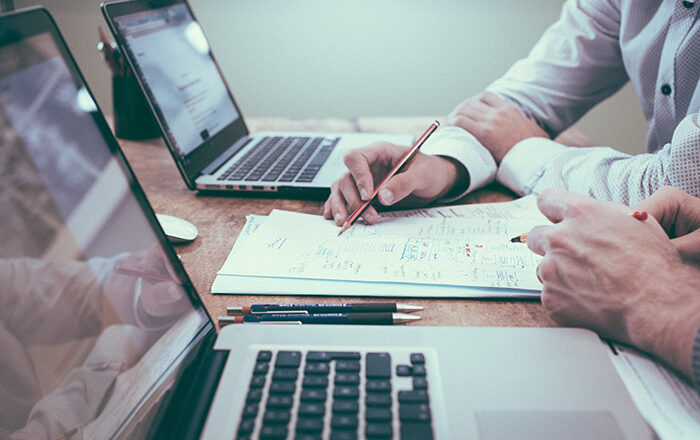 Two business man with their laptops analyzing a paper document.